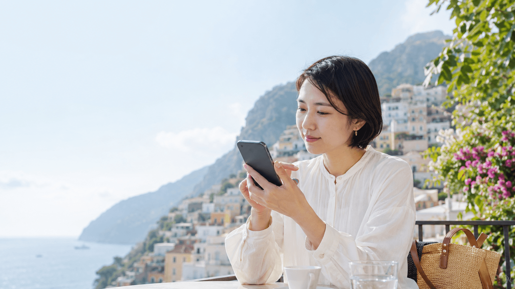 海外の海辺の街を望むテラスでスマートフォンを操作する旅行者
